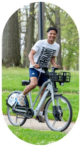 Young African American man wearing a gray tee and blue shorts riding a bicycle in a metropark